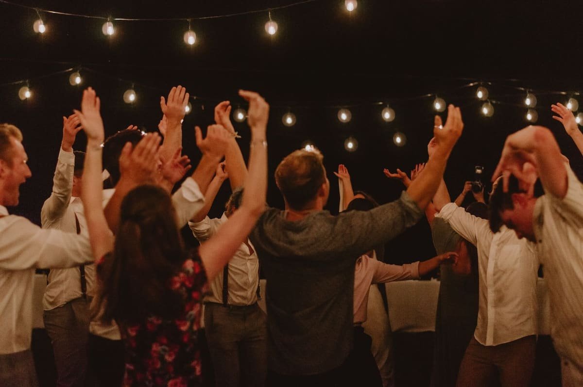 Soirée en extérieur : invités les bras levés sous des guirlandes lumineuses